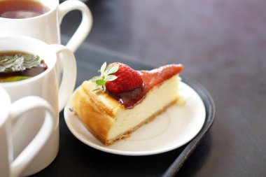 Dilim peynir Kek krem ve taze çilek plaka üzerinde bulanıklık arka plan üzerinde bir fincan çay ile kek. Çay saati kavramı Seçici odak