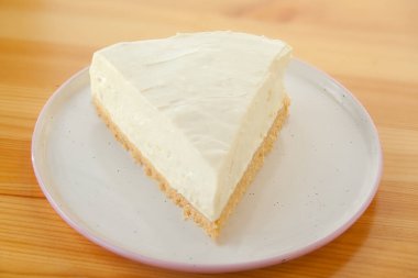 Tahta bir masada beyaz tabakta klasik cheesecake.