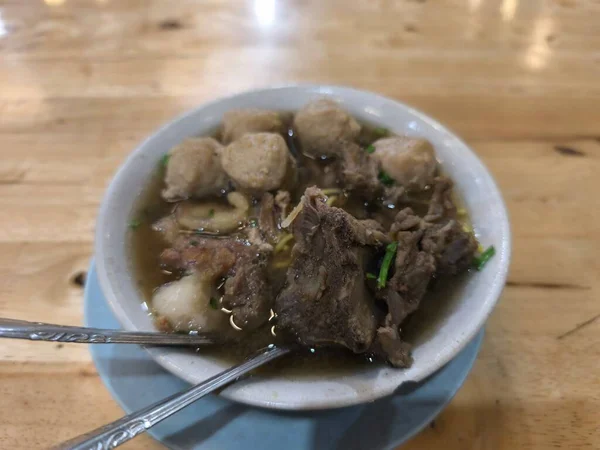 Lezzetli bir kase Endonezya Bakso, leziz biftekli ve erişteli geleneksel köfte çorbası, açık ahşap bir masada servis edilir.