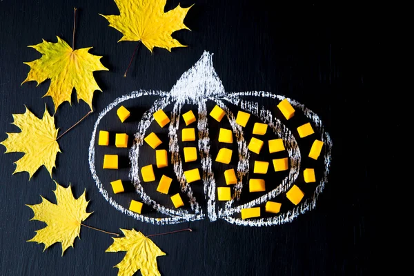 Citrouille dessinée à la craie sur la planche, avec des morceaux de citrouille et des feuilles jaunes — Photo