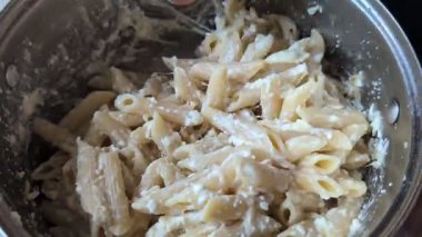 Lezzetli bir porsiyon makarna, bol kremalı peynir sosuyla karıştırılmış, bir tencerede birlikte pişirilmiş.