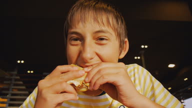 Genç fastfood yeme. Fast food restoran cheeseburger ısırma aç genç çocuğun yakın çekim shot.