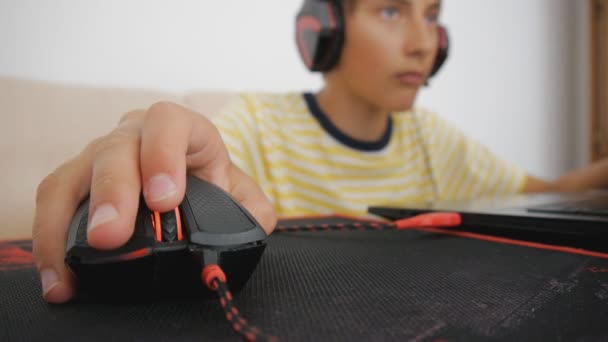 Teenager using laptop. Teen with headphones using wired mouse on pad. Close-up of hand clicking and scrolling computer gaming black and red mouse.