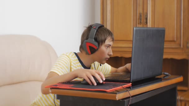 Adolescente che usa il computer portatile. Teen boy con cuffie incollate allo schermo del notebook utilizzando il mouse di gioco del computer . — Video Stock