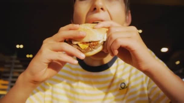 Dospívající jíst fastfood. Detailní záběr teen boy kousání cheeseburger v fast food restaurace. — Stock video