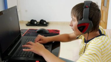 Genç dizüstü bilgisayar kullanarak. Genç çocuk kulaklık bilgisayar oyunu evde dumbbells ile arka planda çalmaya ile. Oyun bağımlılığı ve hypodynamia kavramı.