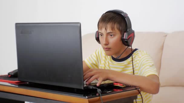 Adolescente usando laptop. Vídeo game adolescente viciado com fones de ouvido colados à tela do notebook pressionando o teclado . — Vídeo de Stock