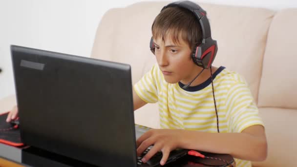 Teenager using laptop. Video game addicted teen with headphones glued to the notebook screen at a loss pressing the keyboard. — Stock Video