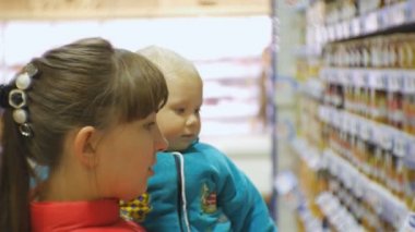 Çekici beyaz kadın kollarında süpermarket holding Baby Bebek Gıda seçimi. Anne Bebek maması alarak yakın çekim çekim bebeğine konuşurken bakkal raf kavanoz.