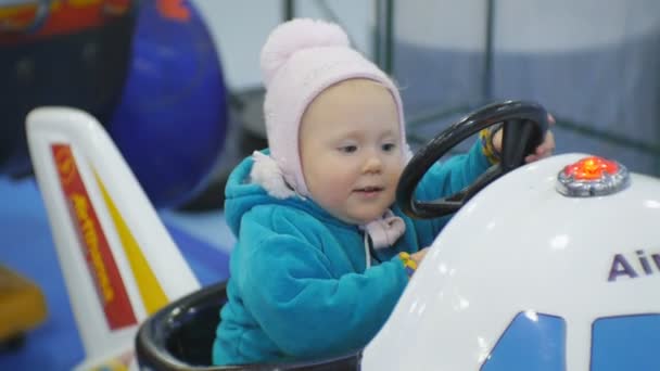 Porträtt av 1,5 år gamla blue eyed babe spelar myntet drivs kiddie ride. Baby flicka vänder ratt av leksak flygplan. — Stockvideo