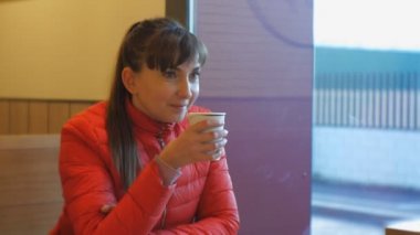 Çekici kadın kafede kahve içiyor. Kahve aroması kokan ve cappuccino bir pencere yakınında yudumlarken zevk kırmızı balonu ceketli beyaz kadın portresi.