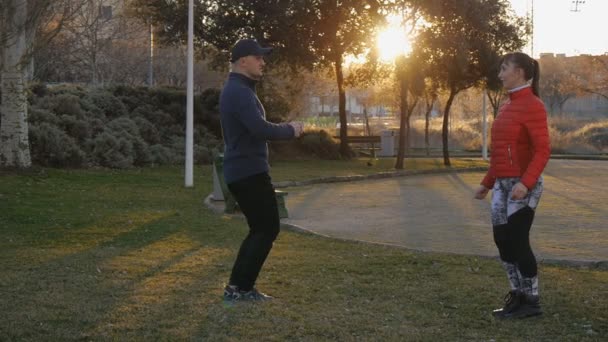 Trening z osobistym trenerem na zewnątrz. Strzał Pan młody instruktor fitness i kobieta robi ćwiczenia lonży naprzeciwko siebie w parku o zachodzie słońca. Trener pokazuje, jak do utrzymania dobrej postawy. — Wideo stockowe