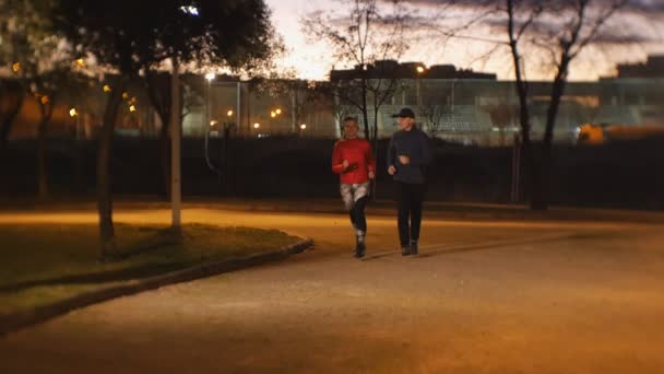 Entraînement avec entraîneur personnel à l'extérieur. Jeune femme séduisante et entraîneur de fitness masculin jogging ensemble dans le parc après le coucher du soleil . — Video
