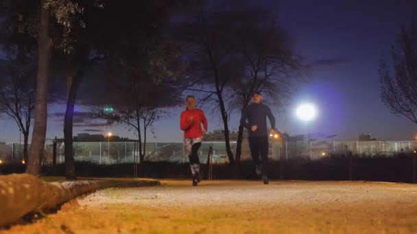 Workout with personal trainer outdoors. Young attractive woman and male fitness coach running together in park at dusk. — Stock Video