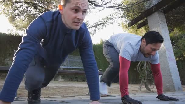 Träning med personlig tränare utomhus. Två manliga idrottare gör plankan knä till armbåge övningar tillsammans i en park som en del av en workout rutin. — Stockvideo