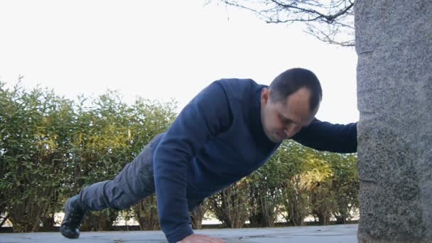 Entrenamiento con entrenador personal al aire libre. Atleta masculino con botas y pantalones de estilo militar haciendo flexiones de brazos levantados en un parque como parte de una rutina de entrenamiento . — Vídeos de Stock