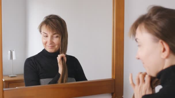 Junge attraktive Frau mit braunen Haaren lächelt und kämmt ihre Haare zu Hause vor dem Spiegel. — Stockvideo