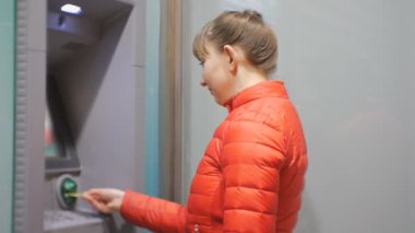 Para kullanan kadın. Kredi kartı Atm ekleme ve PIN kodunu girme kırmızı balonu ceketli çekici genç bayan.