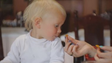 Bebek restoranda yemek yeme. Sarışın mavi gözlü çocuk anneler ellerle ağız yoluyla yiyecek alarak sandalyesi.