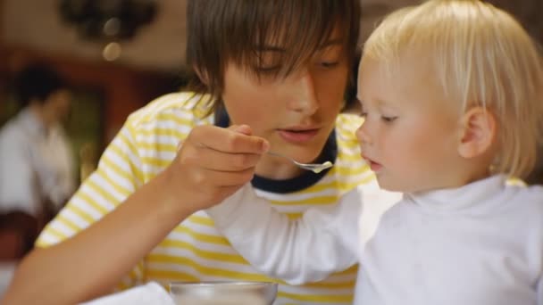 Bébé manger de la nourriture au restaurant. Adolescent nourrit sœur cadette avec une cuillère de crème glacée pour la première fois. Le bébé plisse, repoussant la nourriture offerte . — Video