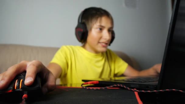Підліток використовує ноутбук вночі. Підліток з навушниками емоційно реагує на рухому прослуховування миші на майданчику. Крупним планом ручна та комп'ютерна ігри чорно-червона миша . — стокове відео