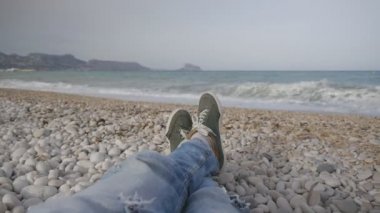 Kot pantolon ve spor ayakkabı bir fırtına sırasında bir çakıl plajı deniz karşı yatan bir adamın bacaklar.