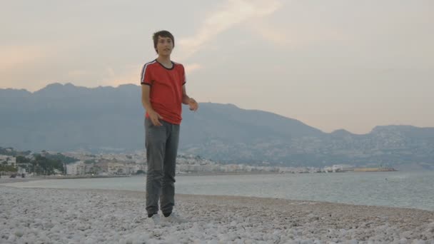 Teenager spielt fliegende Scheibe. Kaukasischer Teenie-Junge fängt emotional fliegende Scheibe an einem leeren Strand in der Nebensaison an der Küste der Berge. — Stockvideo