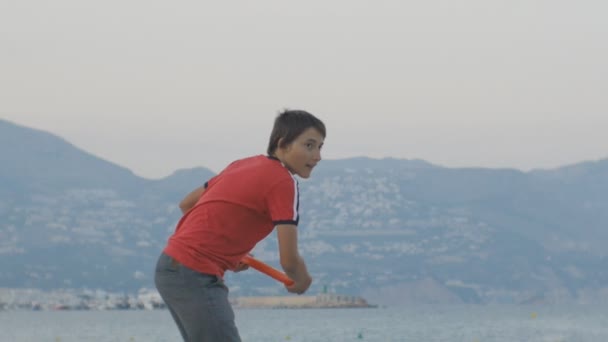 Adolescent jouant disque volant. Caucasien adolescent garçon jette disque volant dans la mauvaise direction et sourit sur une plage vide basse saison sur fond de bord de mer de montagne . — Video