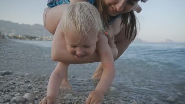 Mamma och baby vid solnedgången lugna havet. Glad kaukasiska småbarn flicka i mammor händer åtnjuter plaskade i havet bevattnar. Begreppet lycklig barndom och familj. — Stockvideo