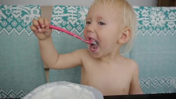 Baby eating yogurt making a mess. Portrait of laughing caucasian blue eyed baby girl eating yogurt. — Stock Video