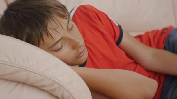 Teenager schlafen auf Couch. Nahaufnahme eines kaukasischen Teenagers in rotem T-Shirt und blauer Jeans, der tagsüber auf einem beigefarbenen Ledersofa schläft. Schlafmangel. — Stockvideo