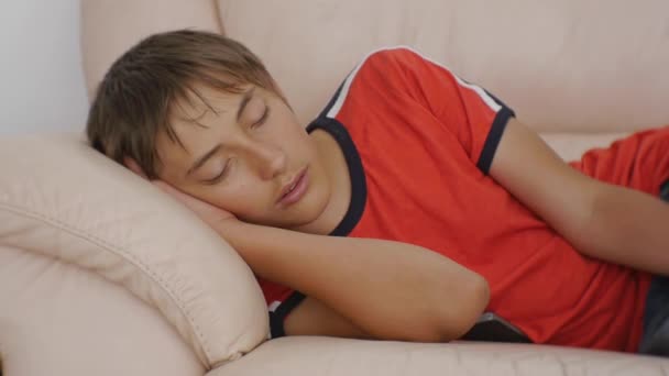 Teenager schlafen auf Couch. Kaukasischer Teenager in rotem T-Shirt und blauer Jeans, der tagsüber auf einem beigefarbenen Ledersofa schläft. Schlafmangel. — Stockvideo