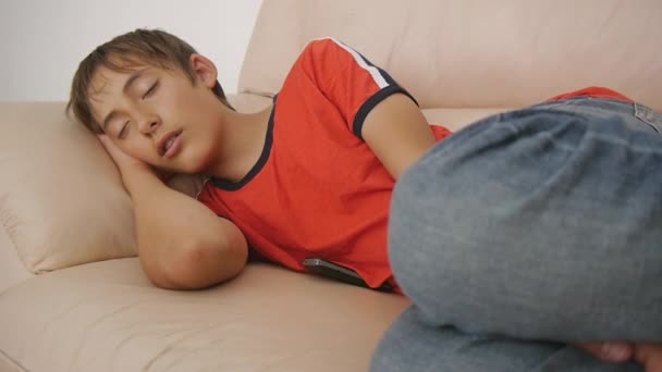 少年睡在沙发上。白人少年男孩穿着红色 t恤衫和蓝色牛仔裤, 白天睡在米色真皮沙发上。睡眠不足. — 图库视频影像