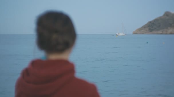 Junge Frau auf dem Meer Hintergrund. Porträt einer kaukasischen braunhaarigen Frau im roten Kapuzenpullover, die auf eine Jacht auf See blickt. — Stockvideo