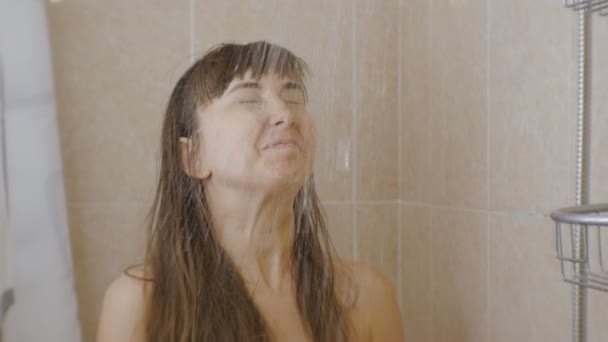 Une femme qui prend une douche. Une jeune femme caucasienne souriante lève les yeux tandis que le ruisseau d'eau commence à verser sur son visage . — Video