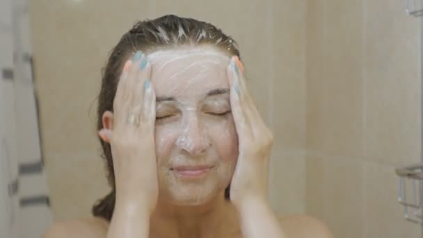 Kobieta pod prysznicem. Zbliżenie: atrakcyjny brązowy włosach kobiety pianotwórczym jej twarzy z peelingiem protokołu soap. — Wideo stockowe