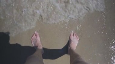 Erkek ayakları ıslak kum deniz dalgaları ile yıkama üzerinde çıplak ayakla ayakta bakış.