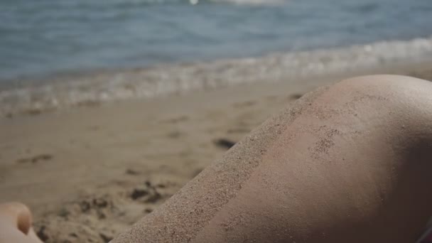 海のそばの砂浜のビーチで横になっている白人の女性のヒップのクローズ アップ. — ストック動画