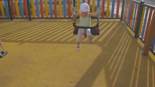 Bambino nel parco giochi. Sorridente bambina in panama cappello divertirsi cavalcando un'altalena catena . — Video Stock