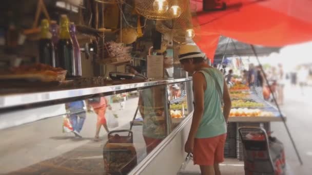 Teen boy in cappello di paglia guarda la vetrina del negozio di gastronomia al mercato rurale di frutta e verdura . — Video Stock