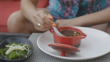 Çekici genç kafkas kadın kil pan Japon restoran açık terasta bir çorba tatma.