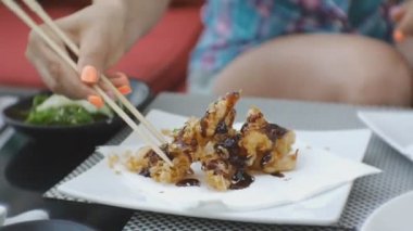 Japon mutfağı çalışan bir kadına. Çekici genç kafkas kadın ısırma Close-up Japon restoran açık terasta yemek çubukları ile alarak tempura karides kızarmış.