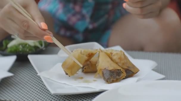 Woman trying japanese cuisine. Close-up of attractive young caucasian woman taking with chopsticks and biting fried spring rolls with vegetables on open terrace of japanese restaurant. — Stock Video