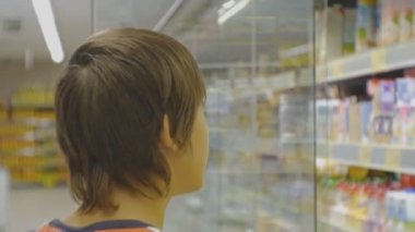 Genç süpermarkette. Arka plan beyaz teen boy kırmızı t-shirt süt tereyağı mağaza buzdolabı seçim içinde raflar.