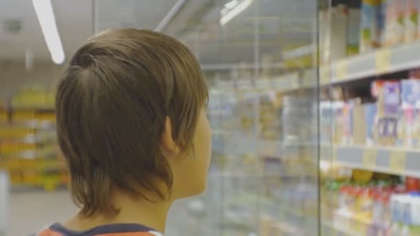 Tiener in de supermarkt. Kaukasische tiener jongen in rode t-shirt kiezen zuivel boter uit de koelkast op winkel rekken achtergrond. — Stockvideo