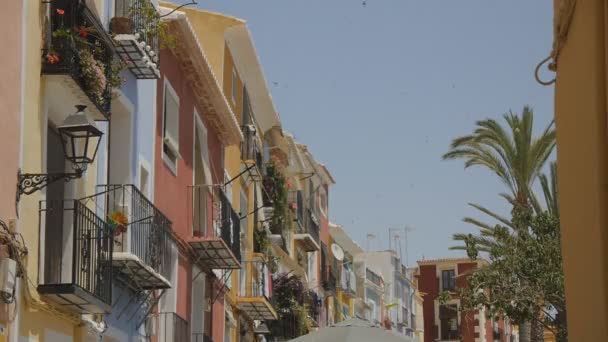 Old-fashioned southern european residential buildings with multi-colored facades. Rotating pinwheel on a balcony and flying swallows in the blue sky. Cinemagraph. — Stock Video