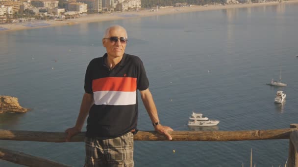 Yaşlı erkek turist emekli oldu. Etkin beyaz gri saçlı komuta sizde dağ deniz kıyısında arka plan üzerinde duran güneş gözlüğü portresi. — Stok video