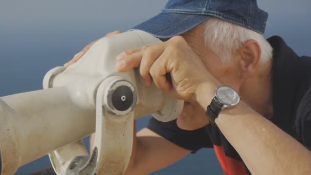 Turista jubilado anciano. Primer plano del hombre mayor de pelo gris caucásico activo en gorra azul mirando al mar en el telescopio turístico desde la cubierta de observación elevada . — Vídeo de stock