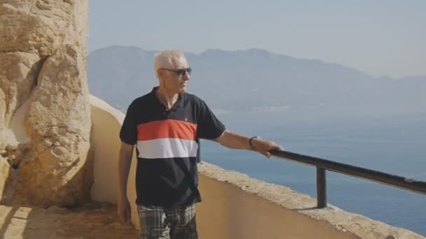 Ältere männliche Rentner Touristen. kaukasische grauhaarige ältere Mann mit Sonnenbrille zu Fuß auf hoher Aussichtsplattform auf Meeresküste Hintergrund. — Stockvideo