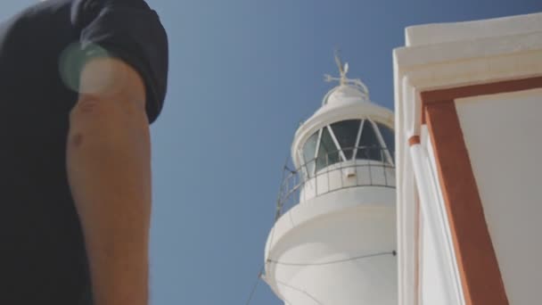 Ältere männliche Rentner Touristen. aktive kaukasische grauhaarige ältere Mann mit Sonnenbrille Blick auf weißen Leuchtturm auf blauem Himmel Hintergrund. — Stockvideo